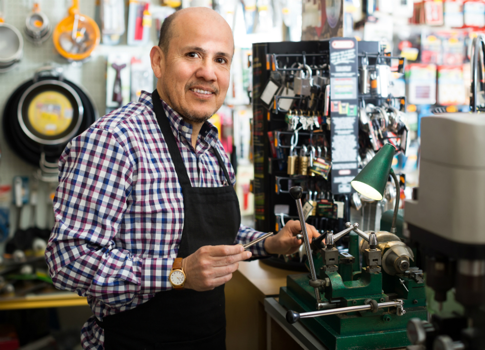 A locksmith at work in his shop, diligently cutting keys. The shop is filled with various tools and key-making equipment.